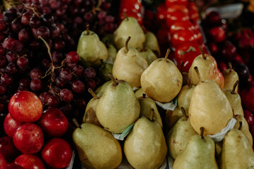 A vibrant display of fresh green pears, red plums, and purple grapes arranged beautifully, showcasing their natural colors and textures in perfect harmony.