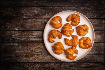 Homemade freshly baked in oven mini croissants on a plate on wooden table, top view. High quality photo