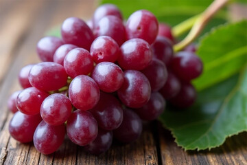 Fototapeta premium A luscious cluster of ripe red grapes, plump and juicy, glistening with a sweet promise of summer's bounty, resting on a rustic wooden surface with vibrant green leaves.