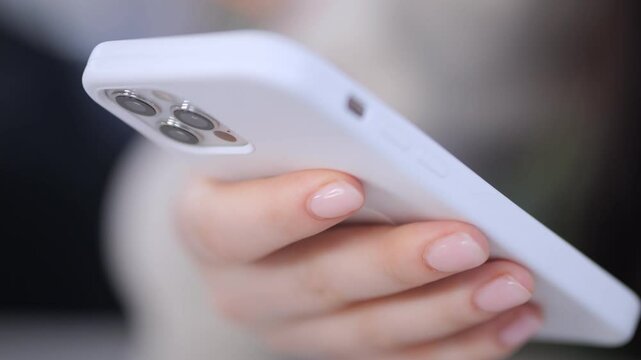 Person is holding a white iPhone in their hand. The phone is the size of a small book and has a white case. The person's hand is holding the phone with a relaxed grip, and their nails are painted