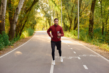 Fototapeta premium Stylish young man jogging through a vibrant autumn park pathway, embracing fitness and fashion