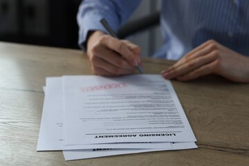 Woman signing licensing agreement document at wooden table indoors, closeup