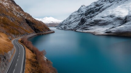 A breathtaking aerial shot of a narrow winding road tracing the curves of a crystal-clear blue lake, snow-capped mountains in the background, relaxing tourism concept