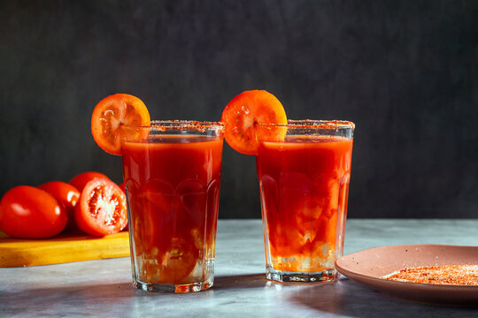 Two Bloody Mary cocktails in glass served with tomato slice and salt on dark background. Red cocktail. Alternative taste. Dirty dump drink