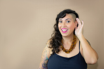 Excited woman with tattoos cupping her ear, acting playful. She wears a black top and amber...