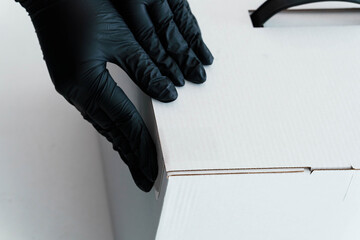 Close-up of Black Gloved Hands Carefully Handling White Cardboard Box Packaging