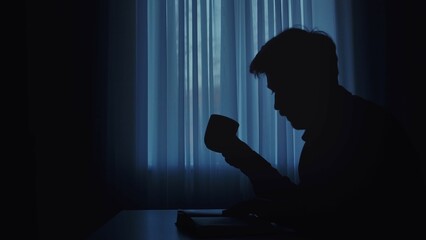 Silhouette of Person Drinking Coffee in Dimly Lit Room