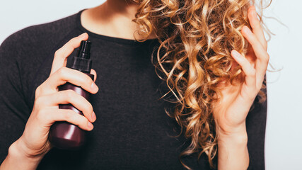 A woman is spraying her hair with a bottle of hair spray