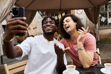 Two handsome men enjoying a delightful afternoon date at a cozy cafe while taking selfies together