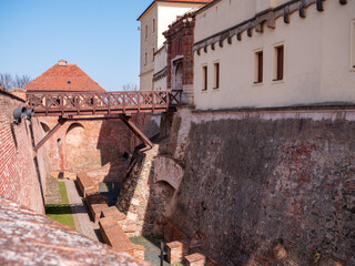 View of Spilberk Castle's empty moat in Brno, Czech Republic, with brick walls, stone paths, and a wooden bridge under a partly cloudy sky.