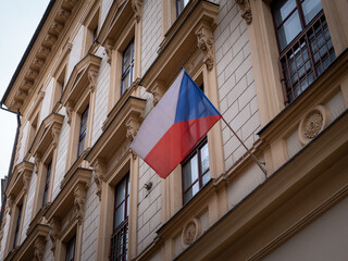 Czech national flag waving on the facade of a historic building with classic architectural details...