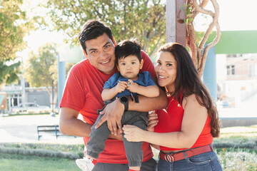 Young family trio smiling in park, parents matching in red