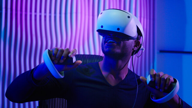 Close up African American gamer user gadget addict modern technology gaming addiction dependency man male guy in cyber futuristic room indoors using VR glasses controllers virtual reality tech helmet