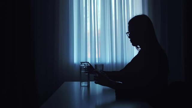 Silhouette of a Person Pouring Water in Low Light Setting