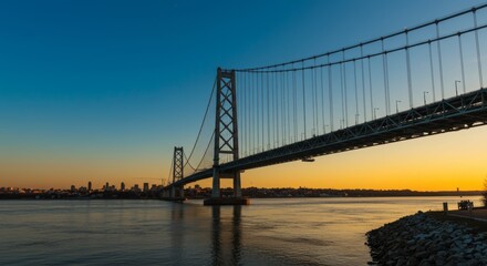 Obraz premium Majestic suspension bridge illuminated by a golden sunset skyline vista