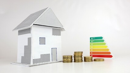 Primo piano di una piccola casa modello con idea di consumo di classe energetica e monete isolate su sfondo bianco