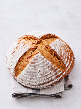 Warm and inviting, a round loaf of freshly baked bread rests atop a soft linen towel, showcasing a beautifully cracked crust and a golden hue from the oven, perfect for sharing