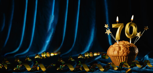 Number 70 gold celebration candle and small stars in sweet cupcake on bright blue velvet background. Concept of celebrating birthday, anniversary. Banner.