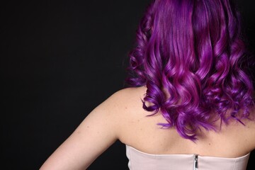 Fototapeta premium Beautiful woman with bright purple hair on black background, back view. Space for text