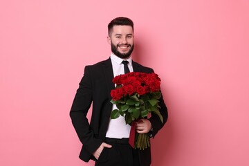 Happy man with bouquet of red roses on pink background