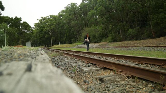 A traveling hobo walks the railway line along an abandoned train station.