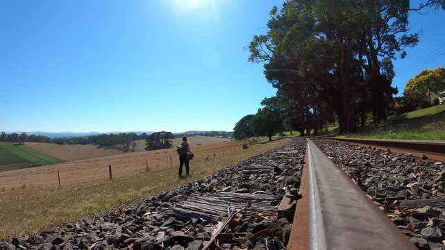 A traveling swagman walks past farm land along a railway in rural Australia.