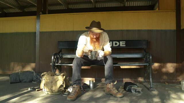 A traveling hobo eats his tinned soup at a historic railway station.