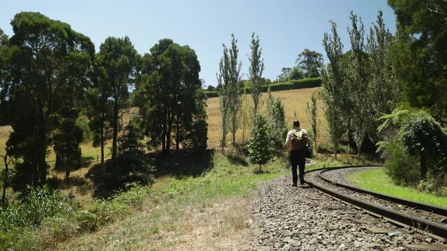 A traveling swagman walks past rural farm land along a historic ralway line in Australia.