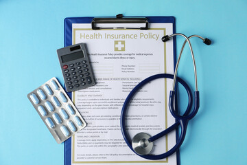Health insurance policy, calculator, pills and stethoscope on turquoise background, flat lay