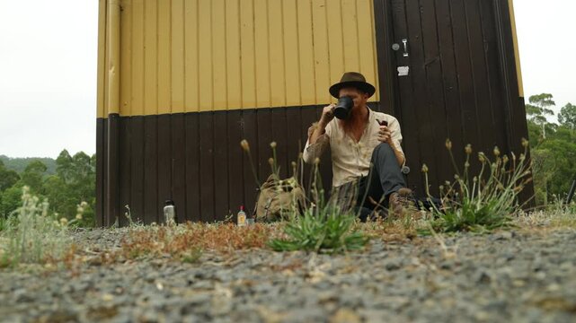 A traveling hobo swagman smokes a pipe at an old railway station in Australia.