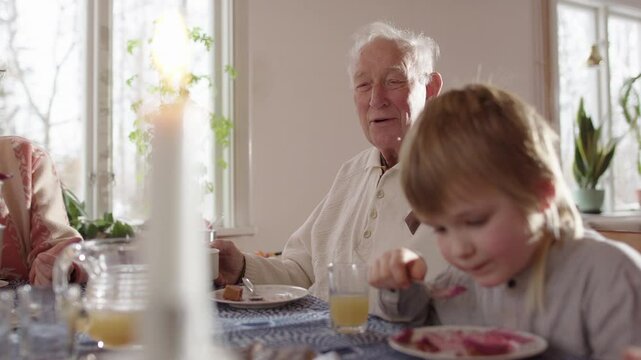 Young boy eats cake next to great-grandfather telling a story at dining table