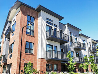 Obraz premium Contemporary apartment building exterior with brick and siding design, featuring balconies and large windows, under a clear blue sky. Modern architecture concept. Ai generative