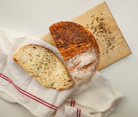 A close view of a freshly baked sourdough bread with a textured, golden crust. Top view of grain   sourdough bread.  Fresh on a wooden board, with a cloth beside it.