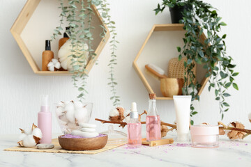 Set of cosmetic products, bath supplies and cotton branch on light table in room