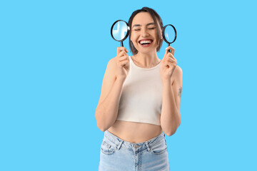 Young woman with magnifiers on blue background