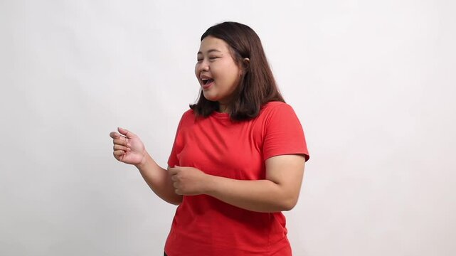 Happy Asian woman standing while pointing sideways on empty space and showing thumbs up. Isolated on white