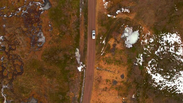 Aerial birdseye view of a travel van on a dirt road with scattered snow coverage