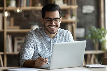 Positive Hispanic entrepreneur man using laptop for working in office, writing notes, smiling, talking on video call. Company manager, businessman watching professional learning webinar