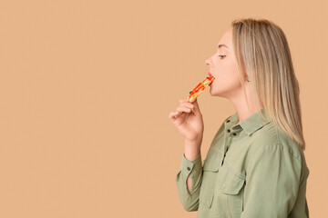 Young woman eating piece of tasty pizza on brown background