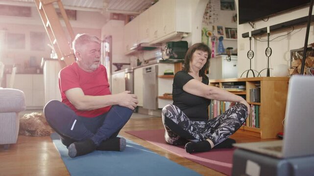 Retired senior married couple sit and follow guided mobility exercises on laptop