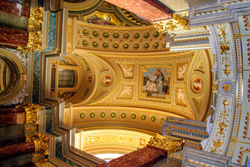 Fototapeta premium The ornate and intricate ceiling displays impressive architectural details with gilded elements, decorative patterns, and religious imagery. Interior wall surface of a basilica.