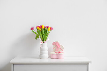Vase with tulips and gift boxes on shelf near light wall. International Women's Day celebration