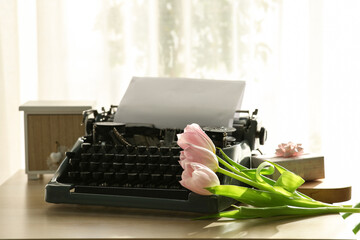 Vintage typewriter with paper sheet, tulips and gift box on wooden table in room