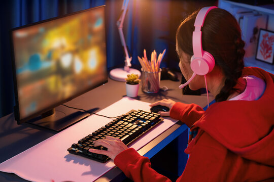 Host channel of young beautiful Asian gaming streamer playing fighting Moba at battle arena game on pc screen with multiplays, wearing pastel headphone at neon digital light modern room. Stratagem.