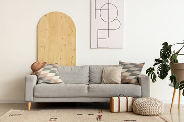 Interior of light living room with grey sofa, pillows, houseplant and picture