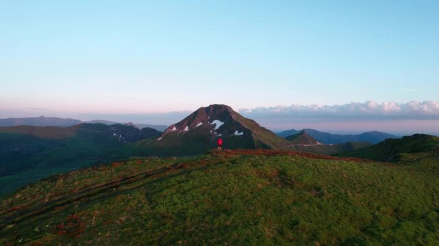 aerial shot revealing Puy Mary Volcano at sunset with a person in red coat looking at the landscape in the foreground from Puy de la Tourte, Cantal departement, Auvergne Rhone Alpes region, France