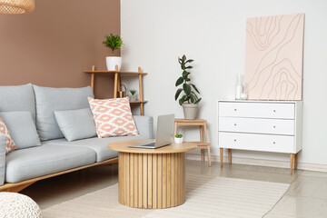 Interior of modern living room with comfortable sofa, coffee table, laptop and picture
