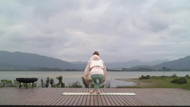 Woman Takes Place on Yoga Mat to Meditate with Lake View - Rear Shot