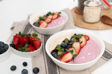 Presented by fruits putting yogurt toppings with strawberry, berry, oats, raisins and chia seed decorated by peppermint in white blow. Pink background. Set of healthy dairy product choice. Pecuniary.