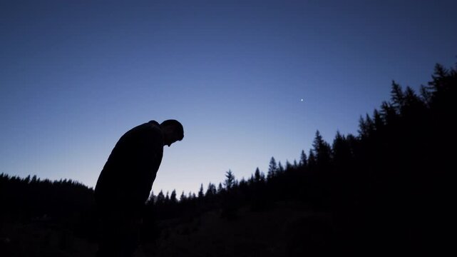 A man climbing a hill pauses for a moment to look at the twilight sky. Against the backdrop of the contour forest, the man admires the first evening star.